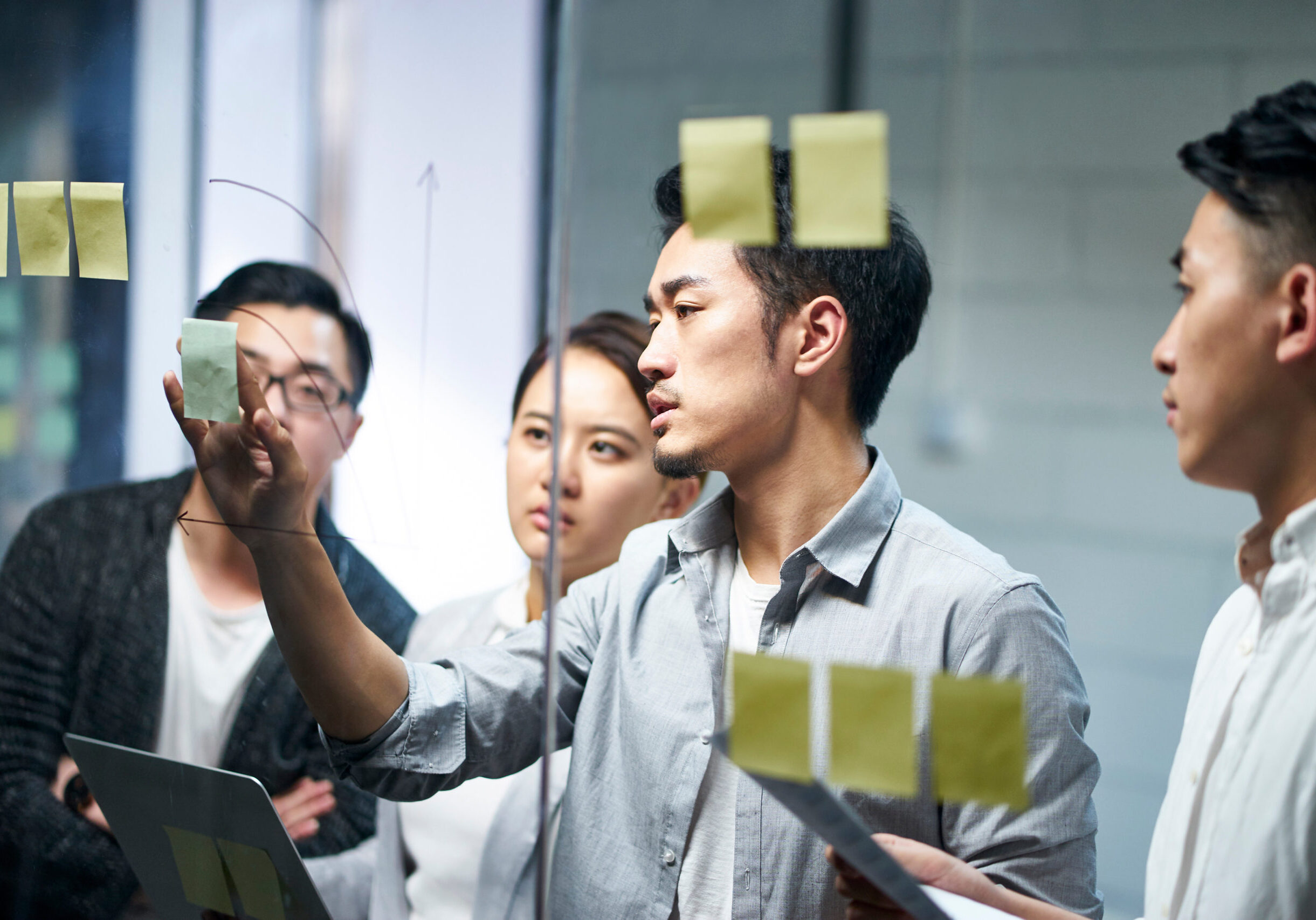 young asian business team people meeting in office young asian entrepreneur of small company putting a adhesive note on glass in office during team meeting formulating business strategies.